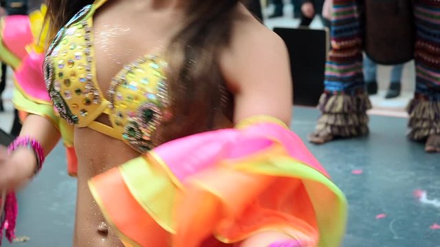 The celebration of the Brazilian carnival in Moscow. Beautiful girl bright colorful carnival costume decorated with rhinestones dancing samba against the background of a yellow building. Half-naked