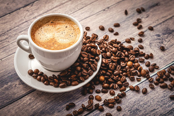 Coffee in a white cup with a saucer and coffee grains on a wooden table background.