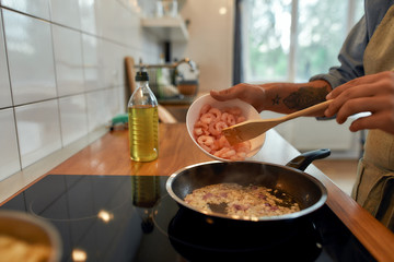 Pursue the flavor. Close up of man adding shrimp to sauteed garlic and onion in the frying pan. Cook preparing dish with seafood. Mediterranean cuisine concept