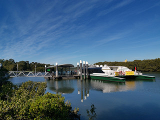 Fototapeta na wymiar Beautiful view of a wharf with boat and reflections of wharf structure, trees and blue sky on water, Parramatta River, Rydalmere Wharf, Rydalmere, Sydney, New South Wales, Australia