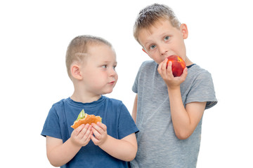 Two boys on a white background,stand.A boy with a burger in his hands looks at a boy biting a peach.The idea is to educate children that fruits and healthy foods can be as delicious as fast food