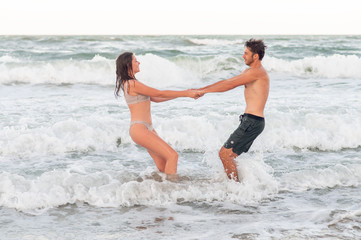 Friends at vacation. Happy young couple having fun in water. man and woman holding hands. Sea with big waves