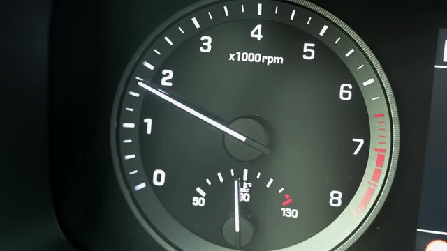 Close up of modern automotive tachometer on black background. The tachometer needle rises.