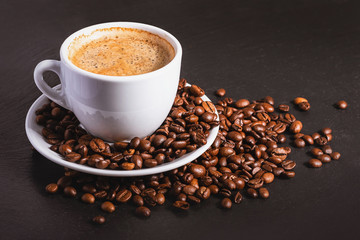 Coffee in a white cup with a saucer and coffee grains on a black background