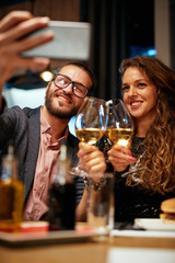 Happy couple sitting in restaurant, toasting with wine an taking selfie.