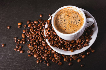 Coffee in a white cup with a saucer and coffee grains on a black background