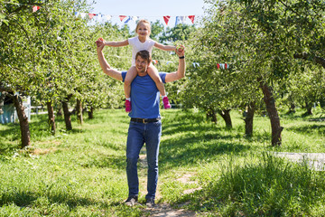 Cheerful man carrying daughter on his shoulders in garden