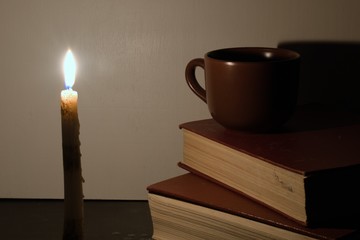 candle light falls on a ceramic mug and old books on a blurred background