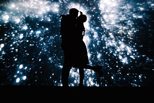 Dark silhouette of kissing couple on background with projection of starry sky