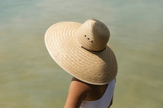 young woman wearing large woven hat by water