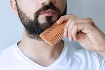 cropped shot of bearded man combing beard with comb isolated on grey