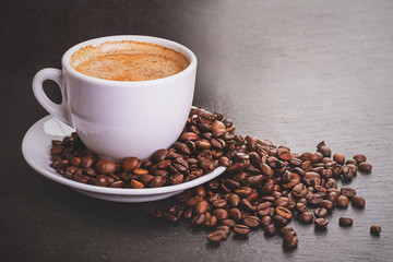 Coffee in a white cup with a saucer and coffee grains on a black background