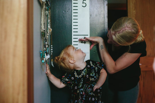 mother measures daughters height on wall growth chart