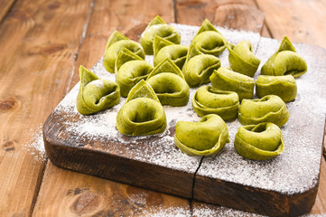 Tortellini e tortelloni typical dishes emilia italy. Food background with homemade raw Italian tortelloni and ingredients for green pesto on wooden background . High angle view. Copy space.
