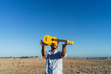 Chico joven sujetando un ukelele amarillo en la playa