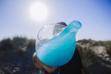 Hombre lanzando bebida azul en la playa con el sol de fondo