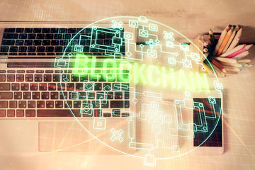 Blockchain theme hologram drawings over computer on the desktop background. Top view. Multi exposure. Concept of cryptoeconomy.