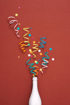 Party with champagne bottle and colorful party streamers on red background top view