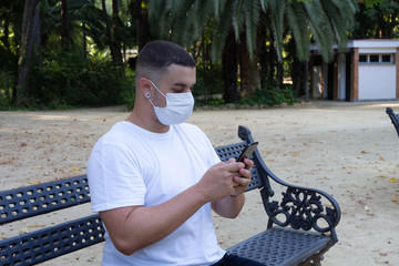 Hombre joven usando el smartphone con una mascarilla sanitaria en la boca respetando las medidas de...