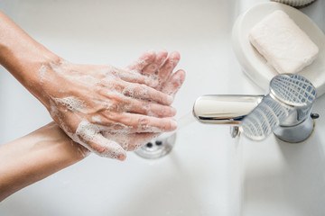 Young woman washes hands in washbasin with soap
