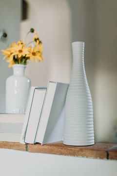 Books, flowers in pot and porcelain bottle on shelf inside home