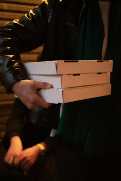 Person carrying three takeaway pizza boxes at night