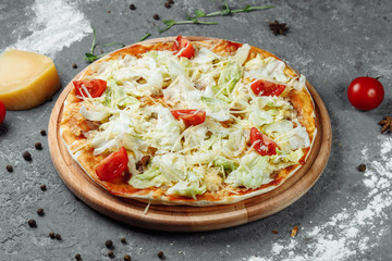 Delicious pizza Caesar style with white sauce, chicken, parmesan, egg, cherry tomatoes and fresh lettuce at wooden background
