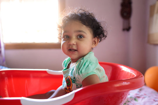 Cute little baby girl sitting in her bathtub on a bed