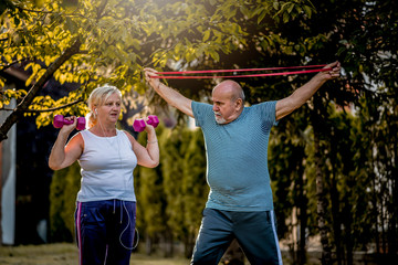 Obraz premium Healthy senior couple exercising with dumbbells and elastic band