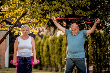 Obraz premium Healthy senior couple exercising with dumbbells and elastic band