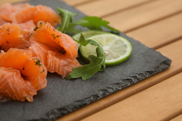 slices of lightly salted salmon on a black plate close up on a wooden table.