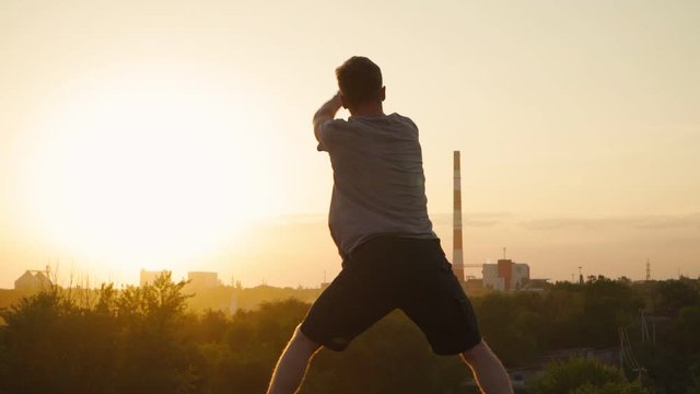 Silhouette of a man practicing martial arts on the background of a beautiful sunset. The guy trains Tai Chi and karate. Art of self-defense. Slow motion
