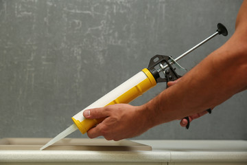 refurbishment in the apartment. kitchen sink sealing close up. worker's hands working with construction sealant gun in the kitchen