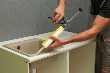 refurbishment in the apartment. kitchen sink sealing close up. worker's hands working with construction sealant gun in the kitchen