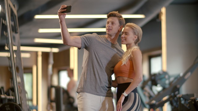 Smiling couple making selfie photo at gym. Fit man taking picture in sport club