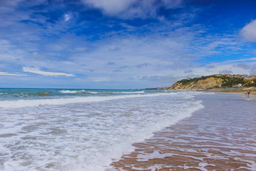 Beach sand rocks and ocean waves against blue coastal skyline