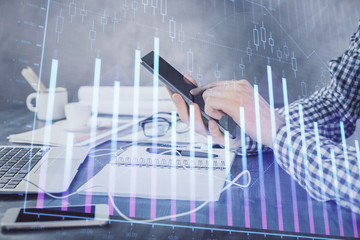 Double exposure of man's hands holding and using a digital device and forex graph drawing. Financial market concept.