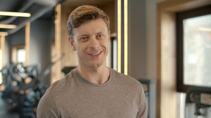 Confident bodybuilder smiling at gym. Sportsman standing in fitness club