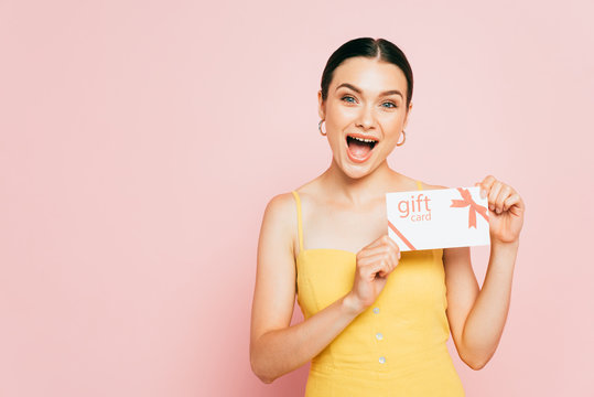 Excited Brunette Young Woman Holding Gift Card Isolated On Pink