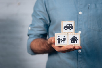 cropped view of man holding wooden cubes with car, family and house in hand