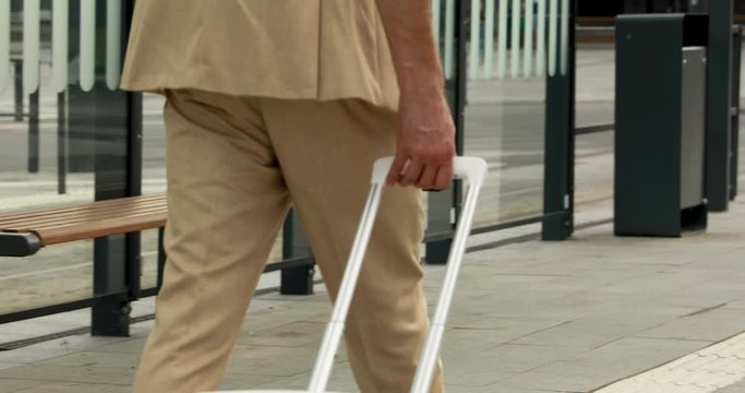 Close up of male traveler in business suit walking on railway station with white suitcase. Successful man having business trip and working meeting at another city.