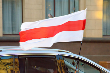 The white-red-white flag of Belarus flies over a driving car