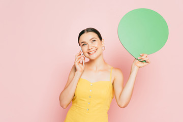 brunette young woman with green blank speech bubble talking on smartphone on pink