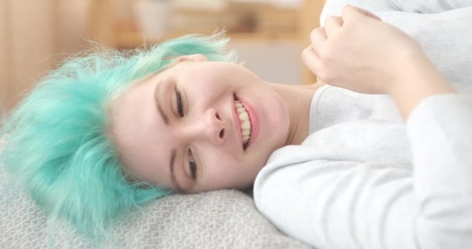 Happy woman with mint hair color lying in bed at home