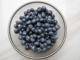 Blueberries placed in a colander on a marble kitchen table.