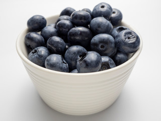 Blueberries in a small white bowl on a white background.