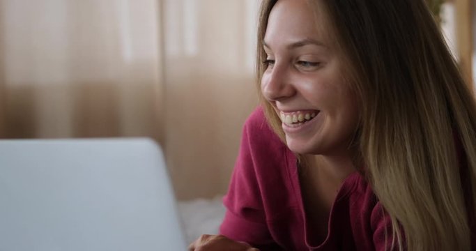 Happy woman feeling satisfied using laptop lying on bed at home