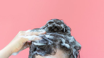 A girl washes her hair with shampoo on pink background, front view