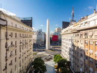 El Obelisco de Buenos Aires enmarcado por dos edificios coloniales y el skyline de la Av. 9 de julio con un cielo azul como fondo.