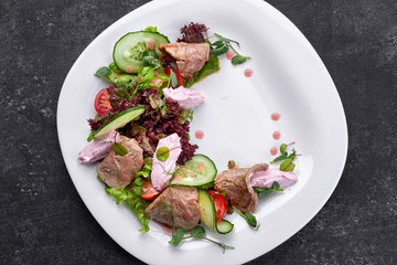 Warm salad with veal and cream cheese, on a white plate and a dark background